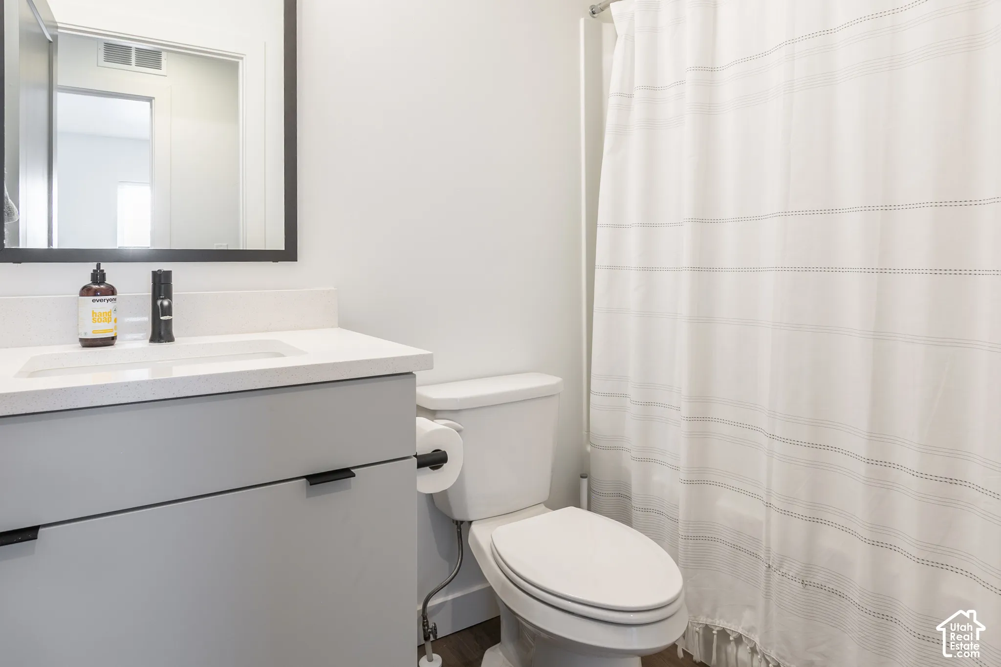 Bathroom featuring a white integrated sink, light gray vanity with black hardware, black framed mirror, and a white toilet