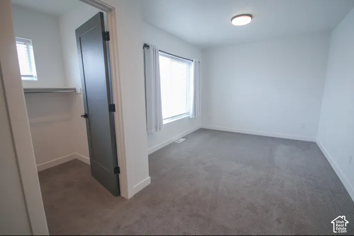 Primary bedroom featuring neutral-toned carpeting, a dark-finished shaker-style door, walk-in closet shelving, and a dual-pane window with natural light