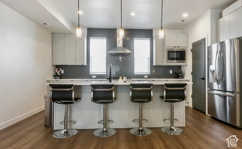Contemporary kitchen featuring a large island with quartz countertop, stainless steel appliances, upper cabinetry, and wood-finish flooring
