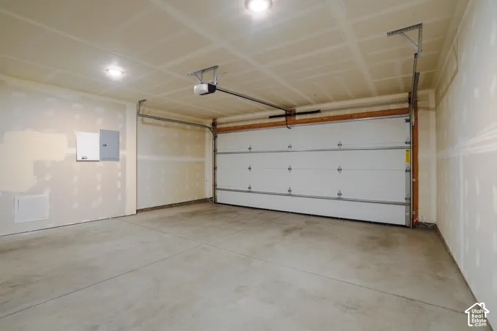Multi-vehicle garage featuring a concrete floor, overhead door, automatic opener, and flush-mount ceiling lighting