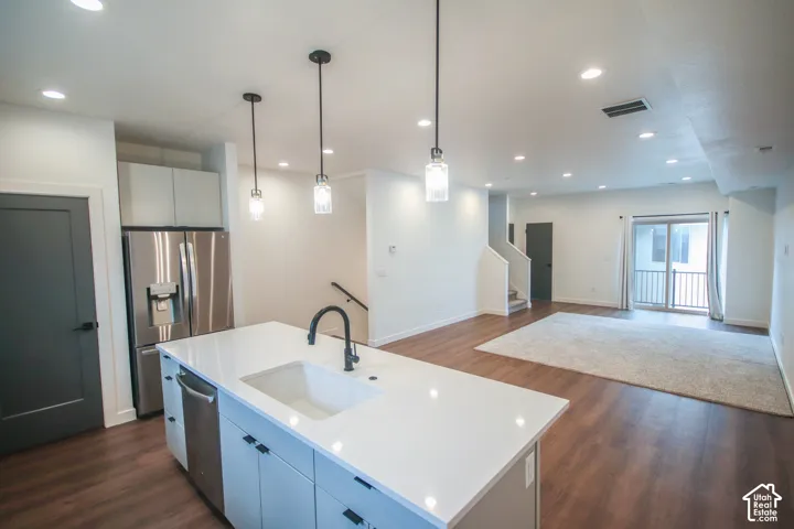 Kitchen featuring a central island with a quartz countertop, white undermount sink, and matte black faucet, accented by three pendant lights and stainless steel appliances