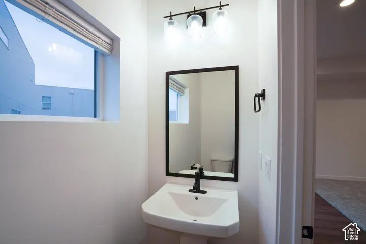 Wall-mounted pedestal sink with a matte black single-handle faucet, rectangular mirror with a dark frame, and a three-light vanity fixture with glass globes