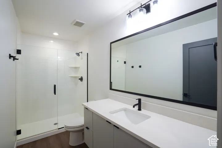 Primary bathroom featuring Euro glass-enclosed shower with tile surround, vanity with a quartz countertop, large rectangular mirror with a dark frame, matte black hardware, and wood-finish flooring