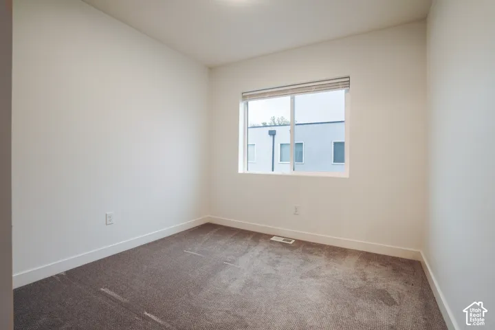 Neutral wall-toned room featuring plush carpeting and a sliding window with integrated blinds