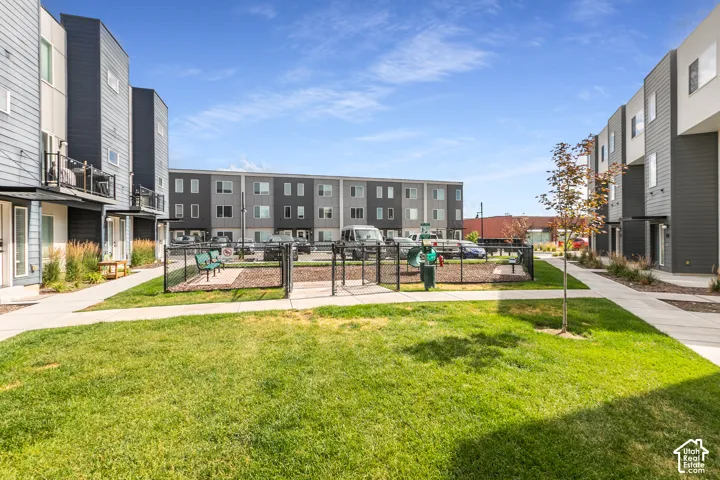 Common area featuring a manicured lawn, concrete walkways, and a fenced recreation space with mulch surfacing