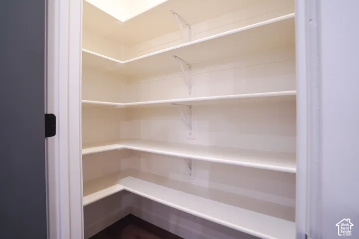 Walk-in pantry featuring multi-tiered white shelving, wall-mounted support brackets, and wood-finish flooring