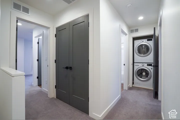 Interior hallway featuring dark-toned paneled closet doors with matte black hardware, recessed ceiling lighting, and a dedicated laundry alcove with a stacked washer and dryer unit