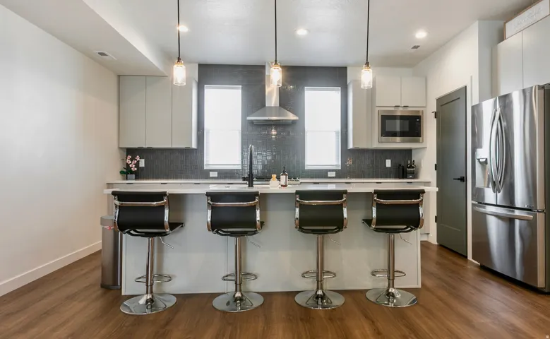 Contemporary kitchen featuring a large island with quartz countertop, stainless steel appliances, upper cabinetry, and wood-finish flooring
