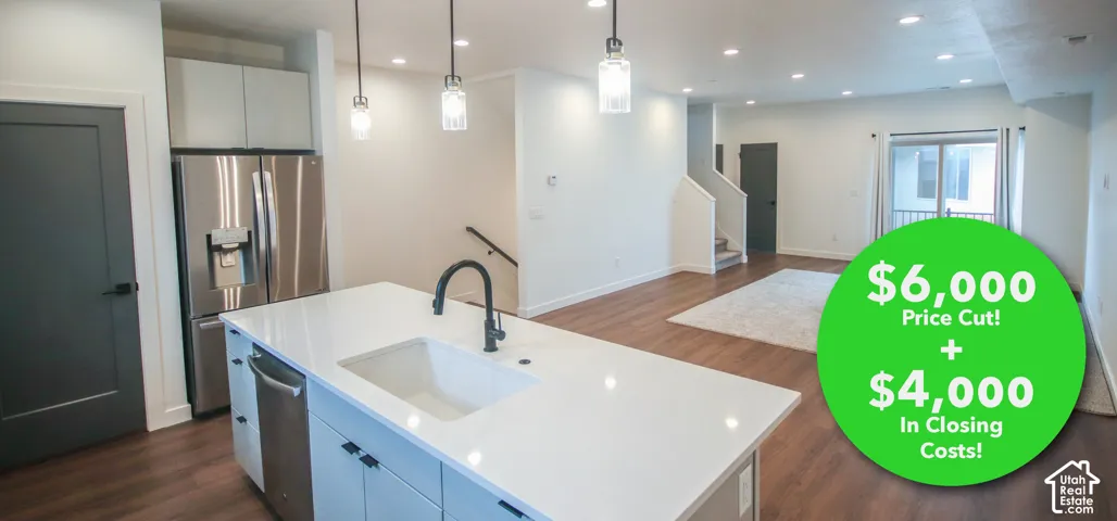 Kitchen island featuring a white countertop, undermount sink, and matte black faucet, complemented by wood-finish flooring, stainless steel appliances, and pendant lighting