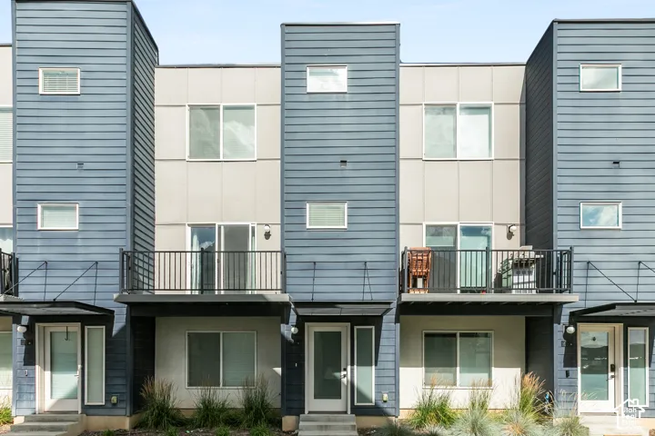 Contemporary architectural exterior featuring horizontal lap siding, panelized wall sections, elevated metal-railing balconies, and minimalist-style entryways