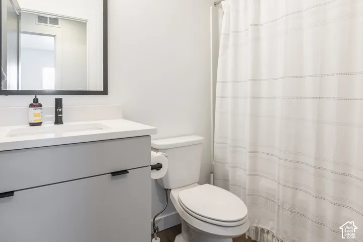 Bathroom featuring a white integrated sink, light gray vanity with black hardware, black framed mirror, and a white toilet