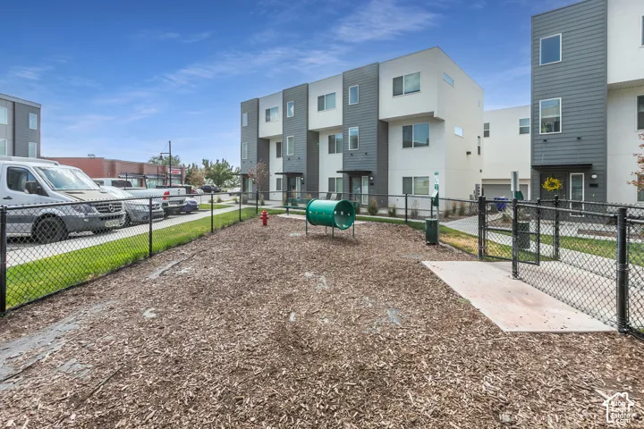 Fenced outdoor area featuring wood chip ground cover, a green play tunnel, and a red fire hydrant