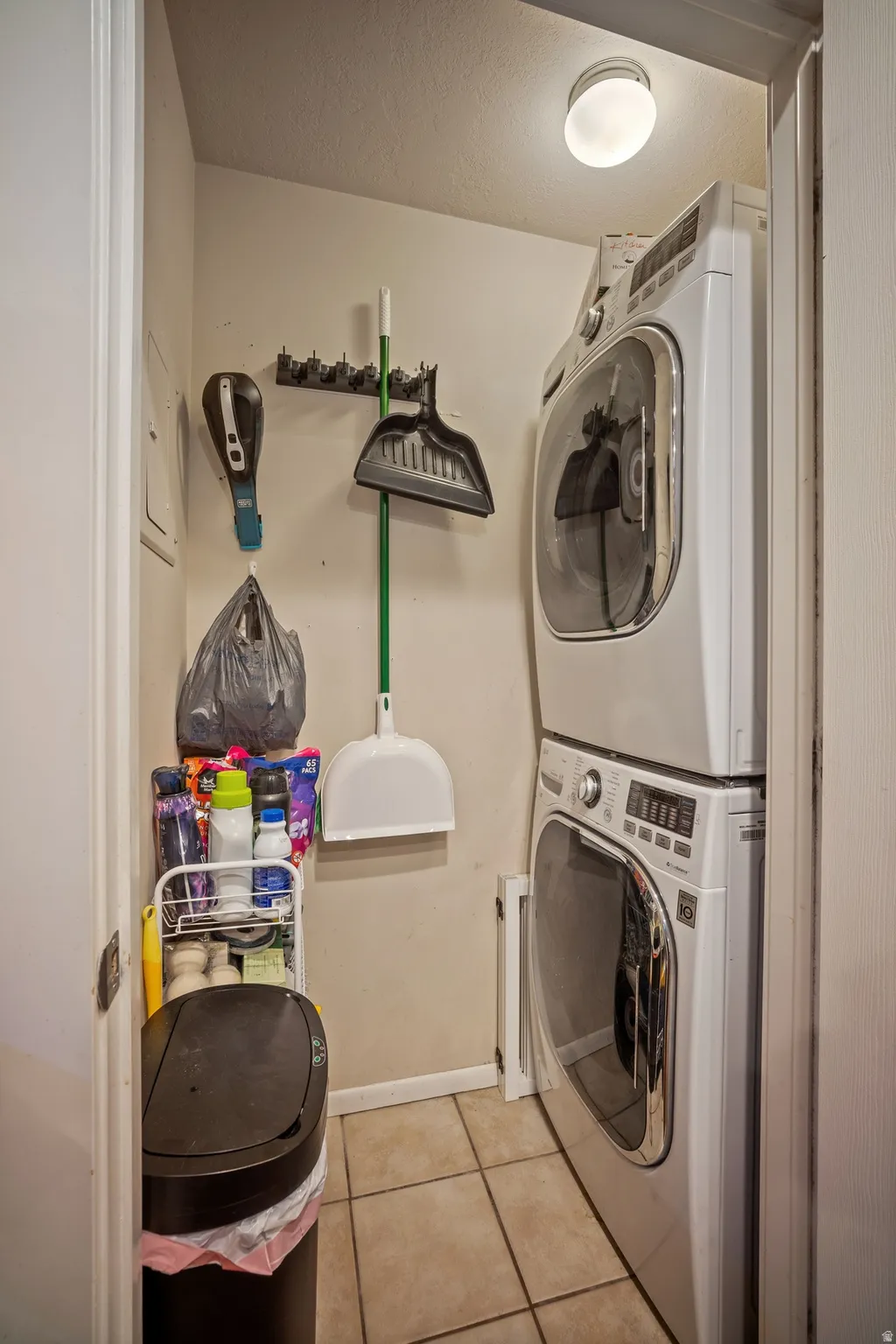 Dedicated laundry area featuring a stacked washer and dryer, tile flooring, and overhead lighting