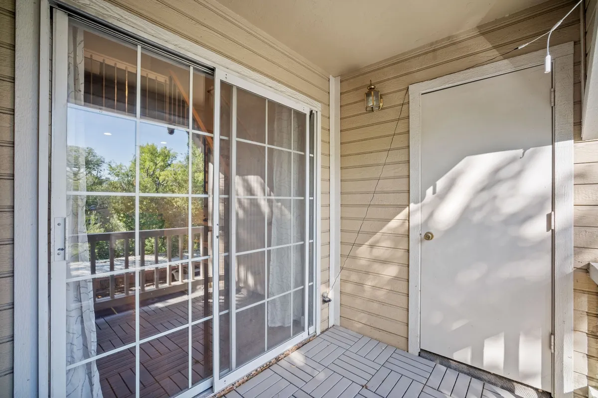 Sliding glass door opening to a private balcony with wooden railing, featuring a neutral exterior siding and light-toned, tile-patterned flooring