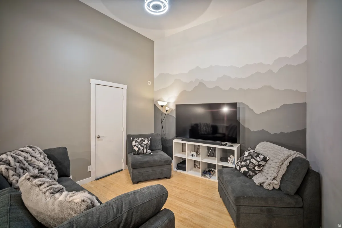 Living space featuring wood-finish flooring, a contemporary ceiling light fixture, a white interior door with dark hardware, and a feature wall with a painted mountain mural