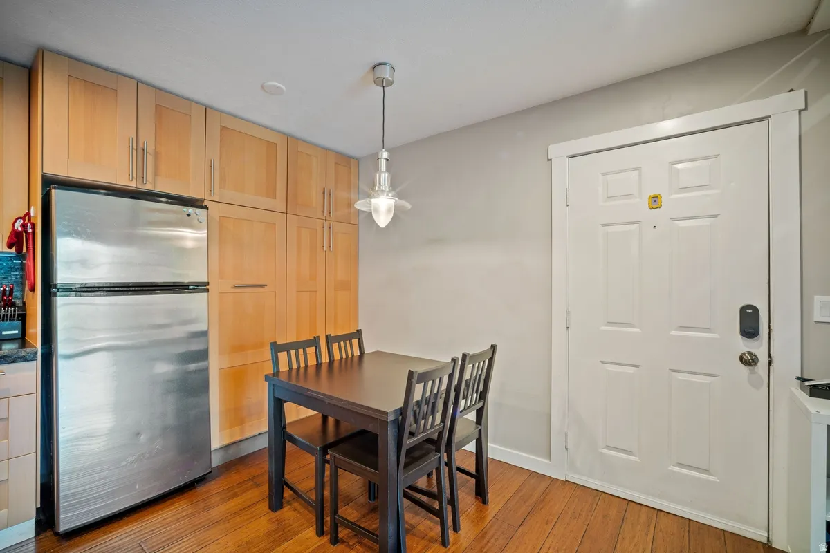 Kitchenette area featuring wood-finish flooring, light wood cabinetry, a stainless steel refrigerator, and a contemporary pendant light fixture