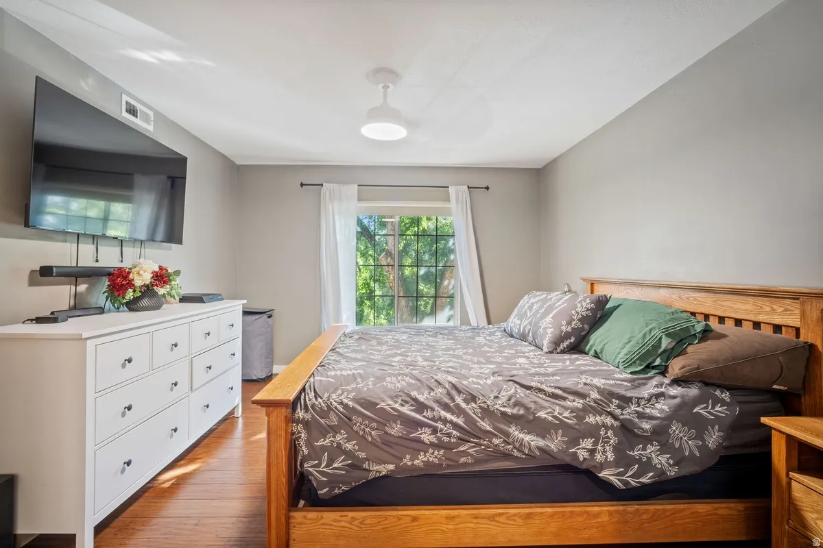 Bright bedroom featuring wood-finish flooring and a single window with white curtains
