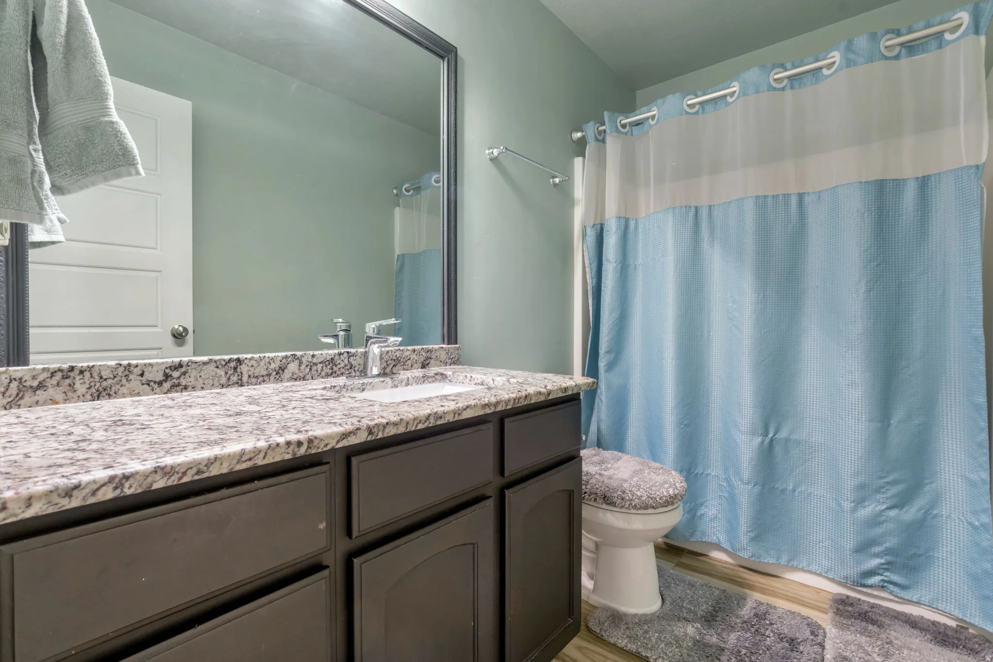 Bathroom featuring a dark wood vanity with a light-toned granite countertop, an integrated sink, and a framed mirror
