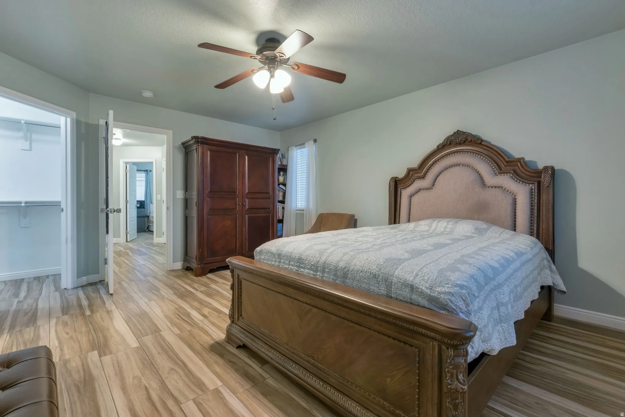 Spacious bedroom featuring wood-finish flooring, a ceiling fan with integrated lighting, and a walk-in closet with built-in shelving