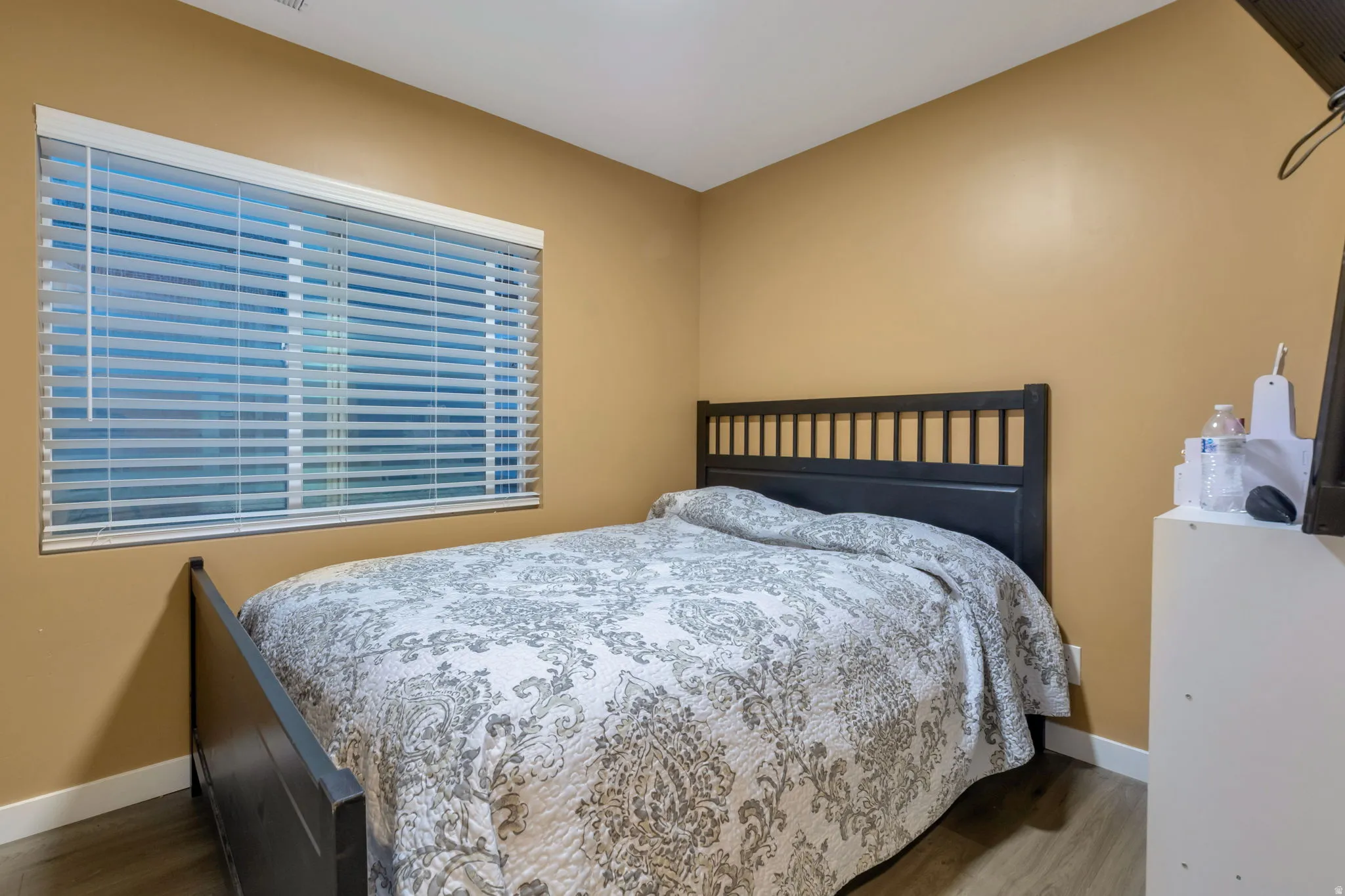 Bedroom featuring a large window with horizontal blinds, warm-toned walls, and wood-finish flooring