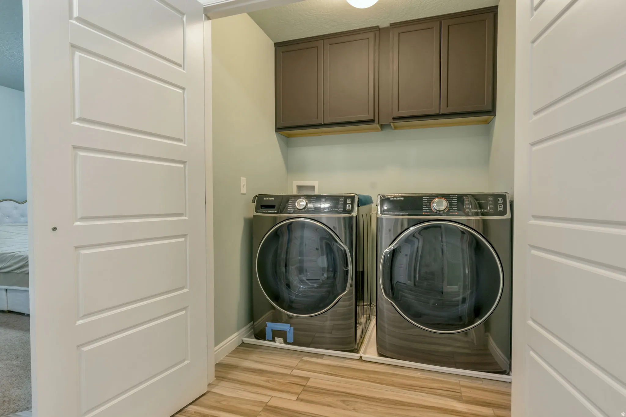 Dedicated laundry area featuring wood-finish flooring and upper cabinetry