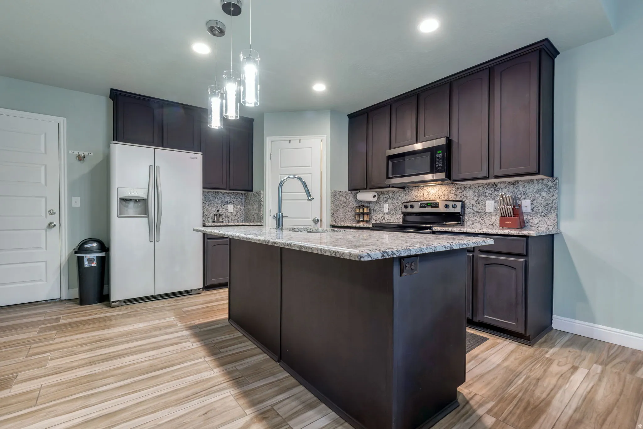 Kitchen featuring a central island with a sink, granite countertops, and dark cabinetry