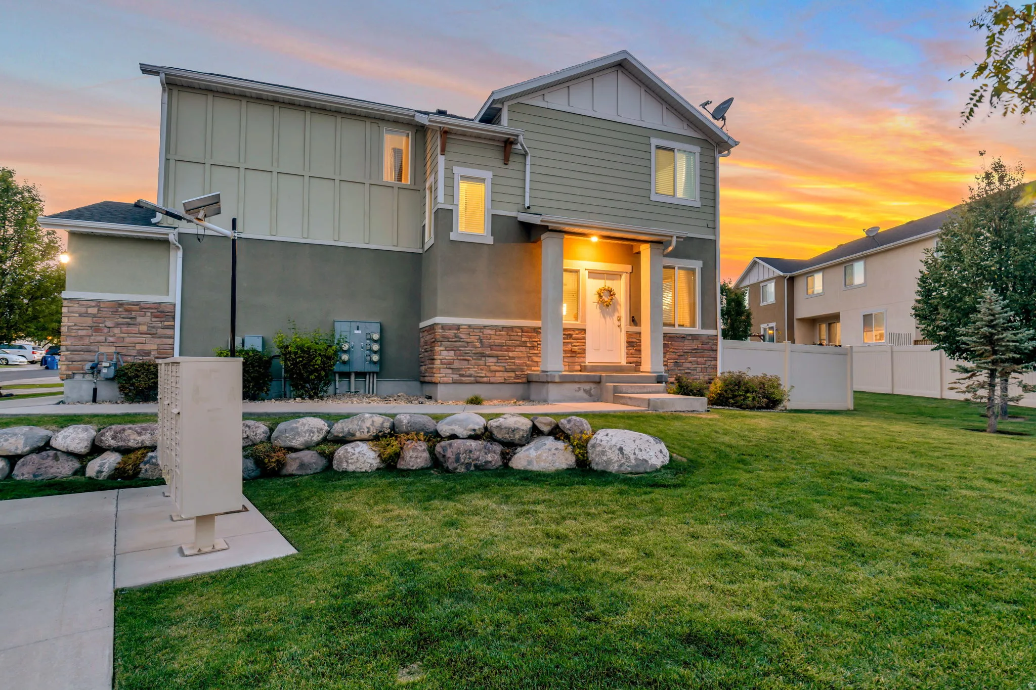 Contemporary multi-story exterior featuring a covered front porch with pillar supports, stone veneer accents, siding, and a manicured lawn with a rock border