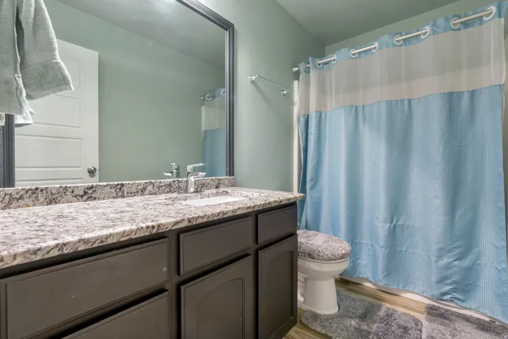 Bathroom featuring a dark wood vanity with a light-toned granite countertop, an integrated sink, and a framed mirror