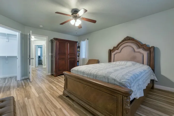 Spacious bedroom featuring wood-finish flooring, a ceiling fan with integrated lighting, and a walk-in closet with built-in shelving