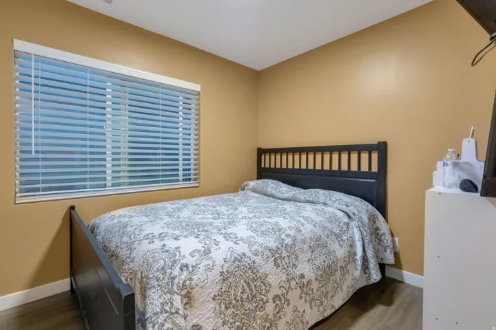 Bedroom featuring a large window with horizontal blinds, warm-toned walls, and wood-finish flooring