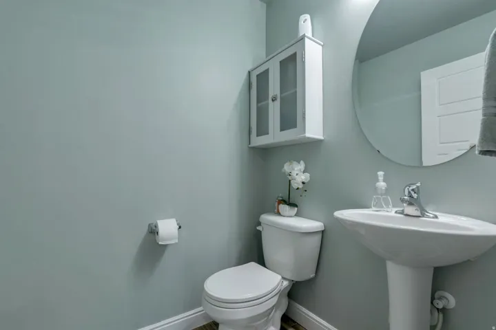 Pedestal sink with chrome faucet, circular wall mirror, and wall-mounted storage cabinet with frosted glass panels