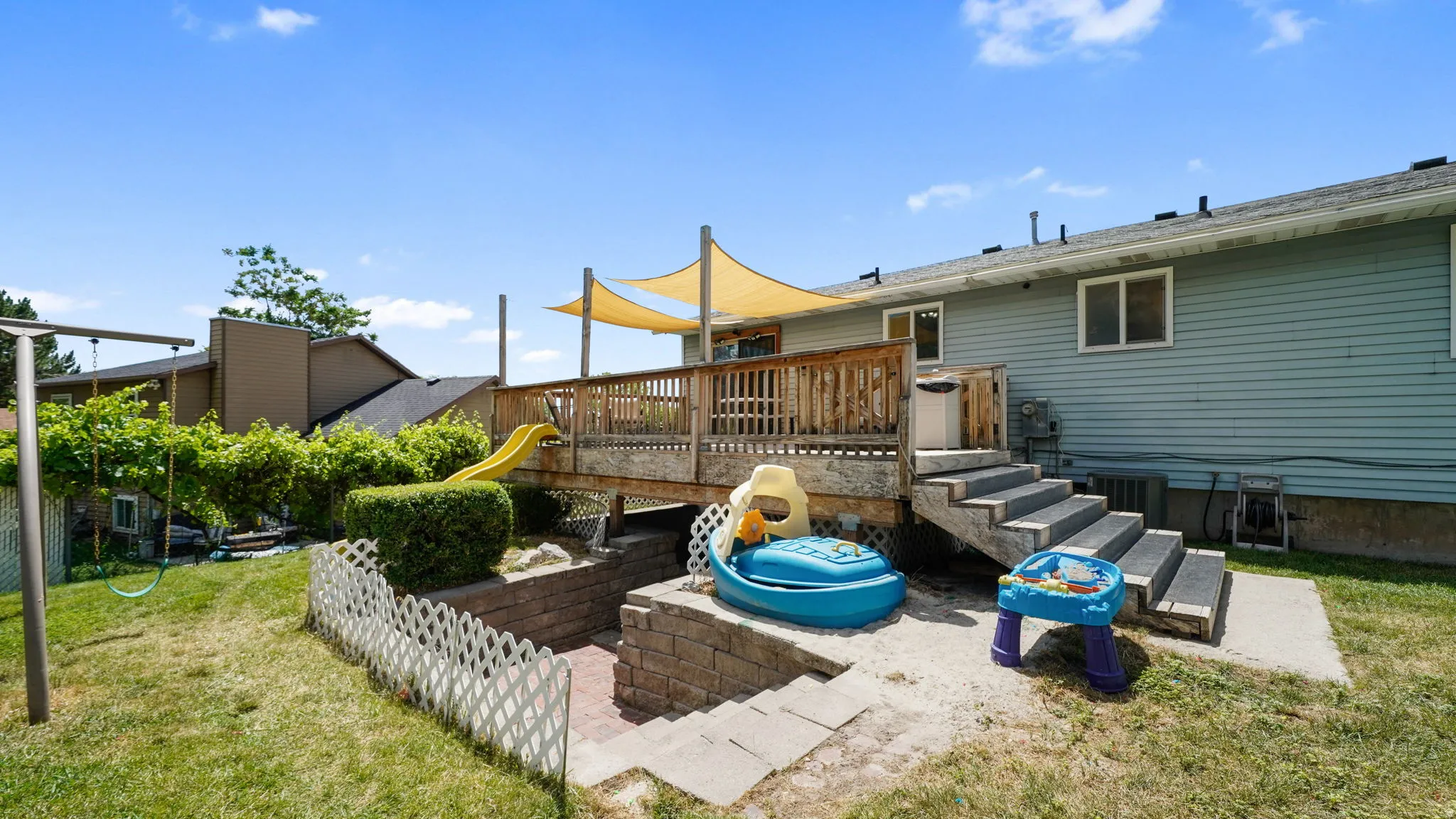 Expansive backyard featuring a multi-level wood-finish deck with a sunshade, a swing set, and mature landscaping