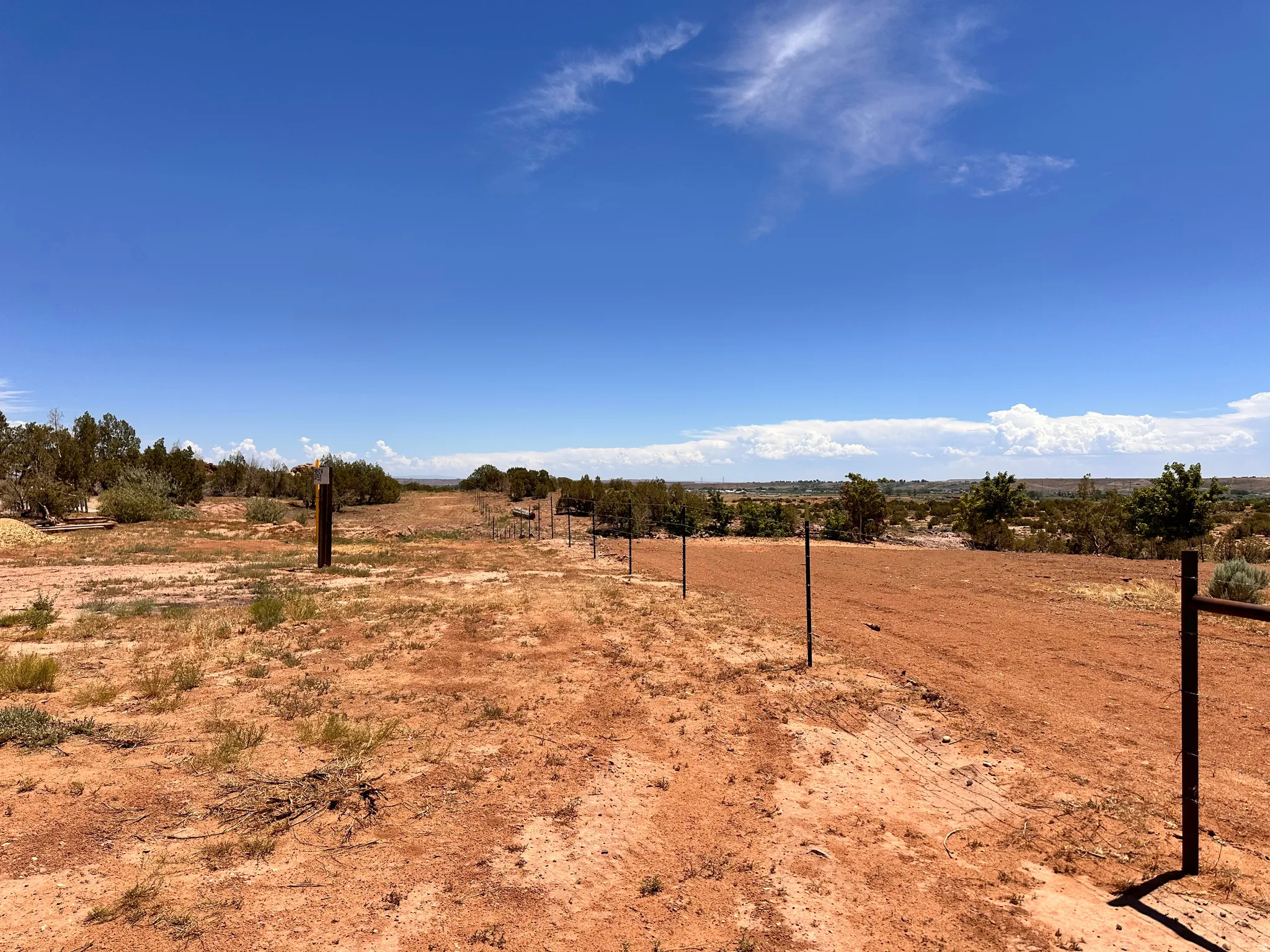 Expansive undeveloped land featuring a clear blue sky, natural desert vegetation, and a partial fence line