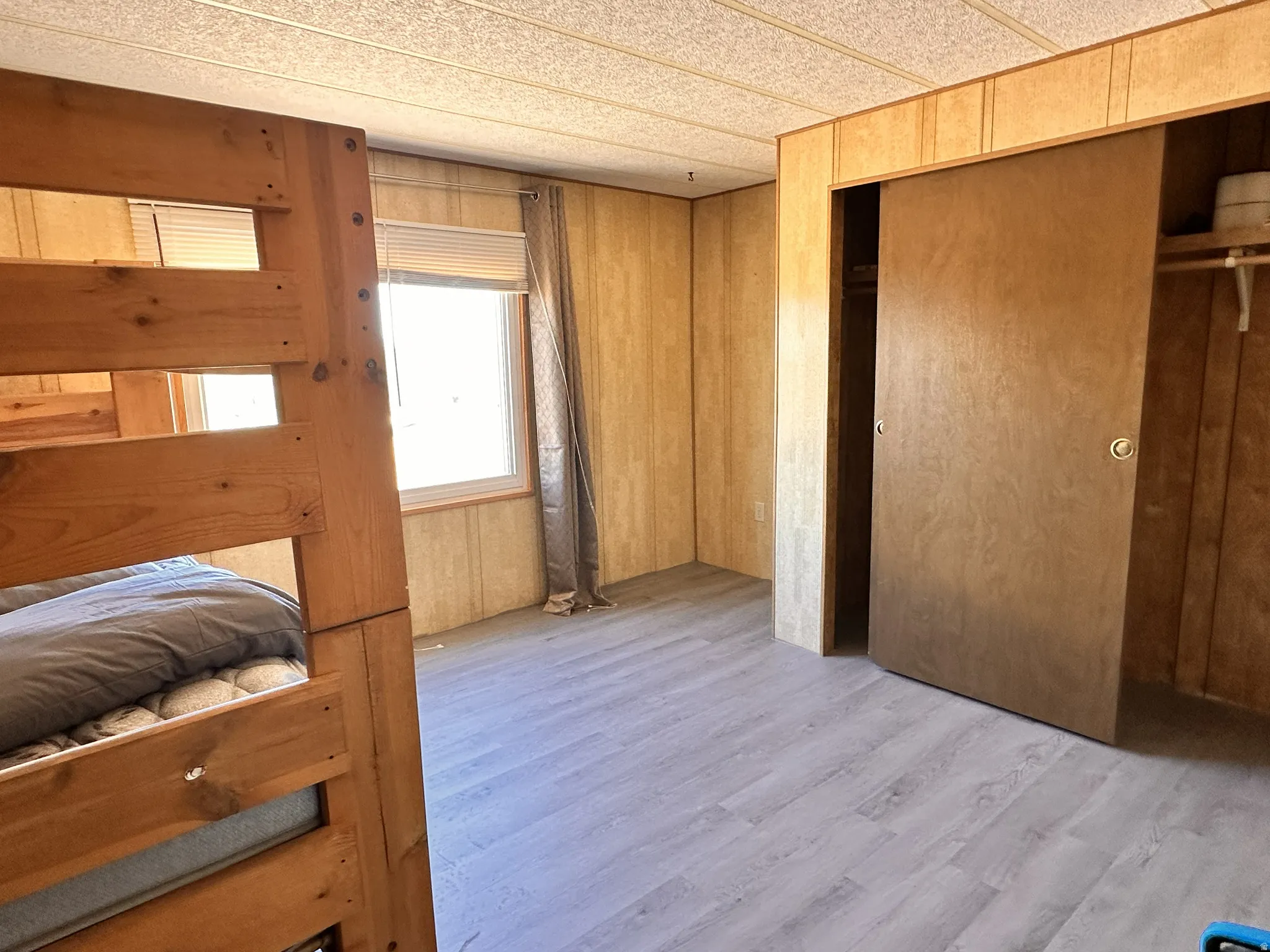 Room featuring wood-finish paneling, light wood-finish flooring, and a window with blinds