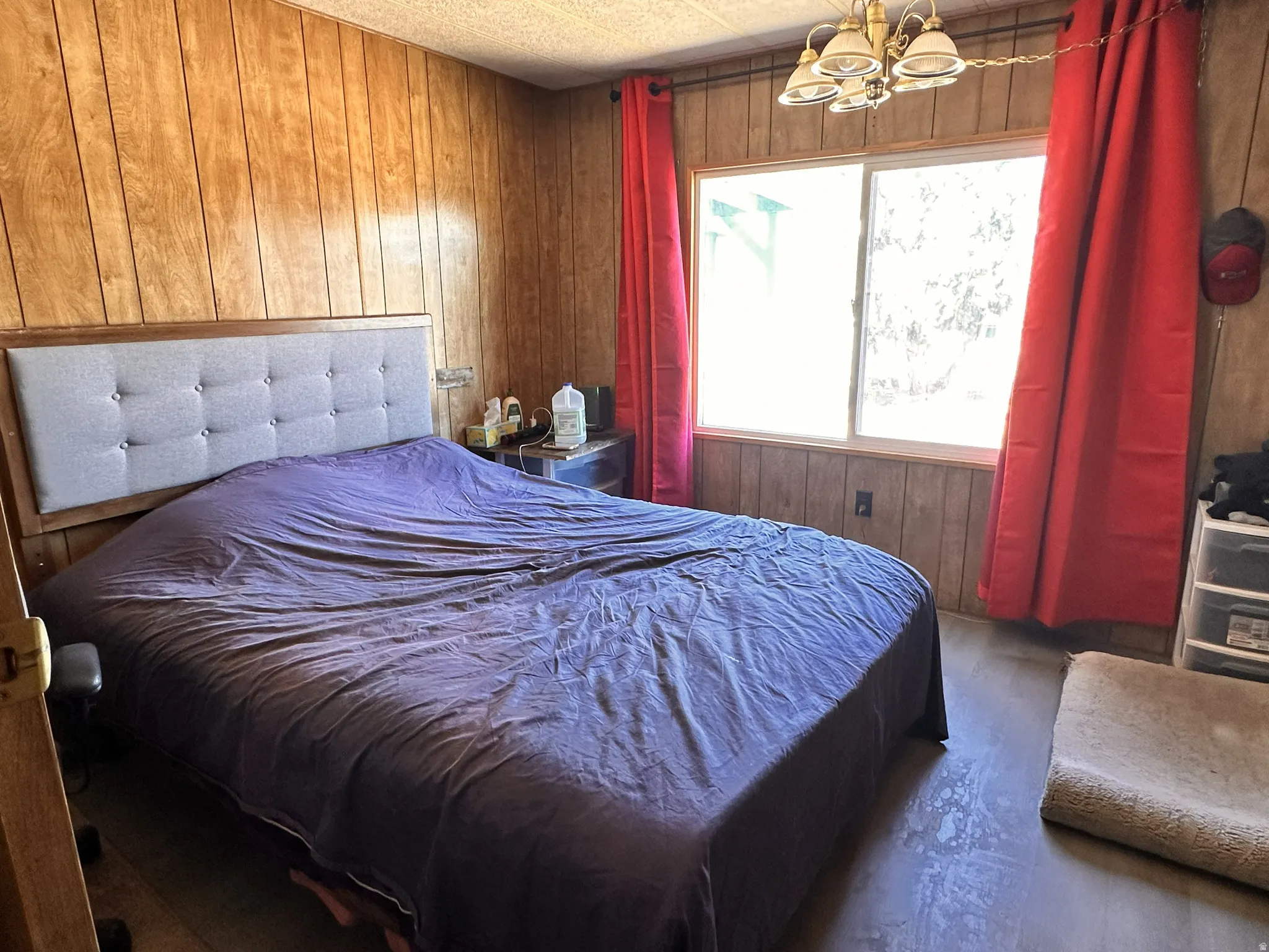 Wood-paneled room featuring a window with a chandelier-style ceiling light fixture, and wood-finish flooring