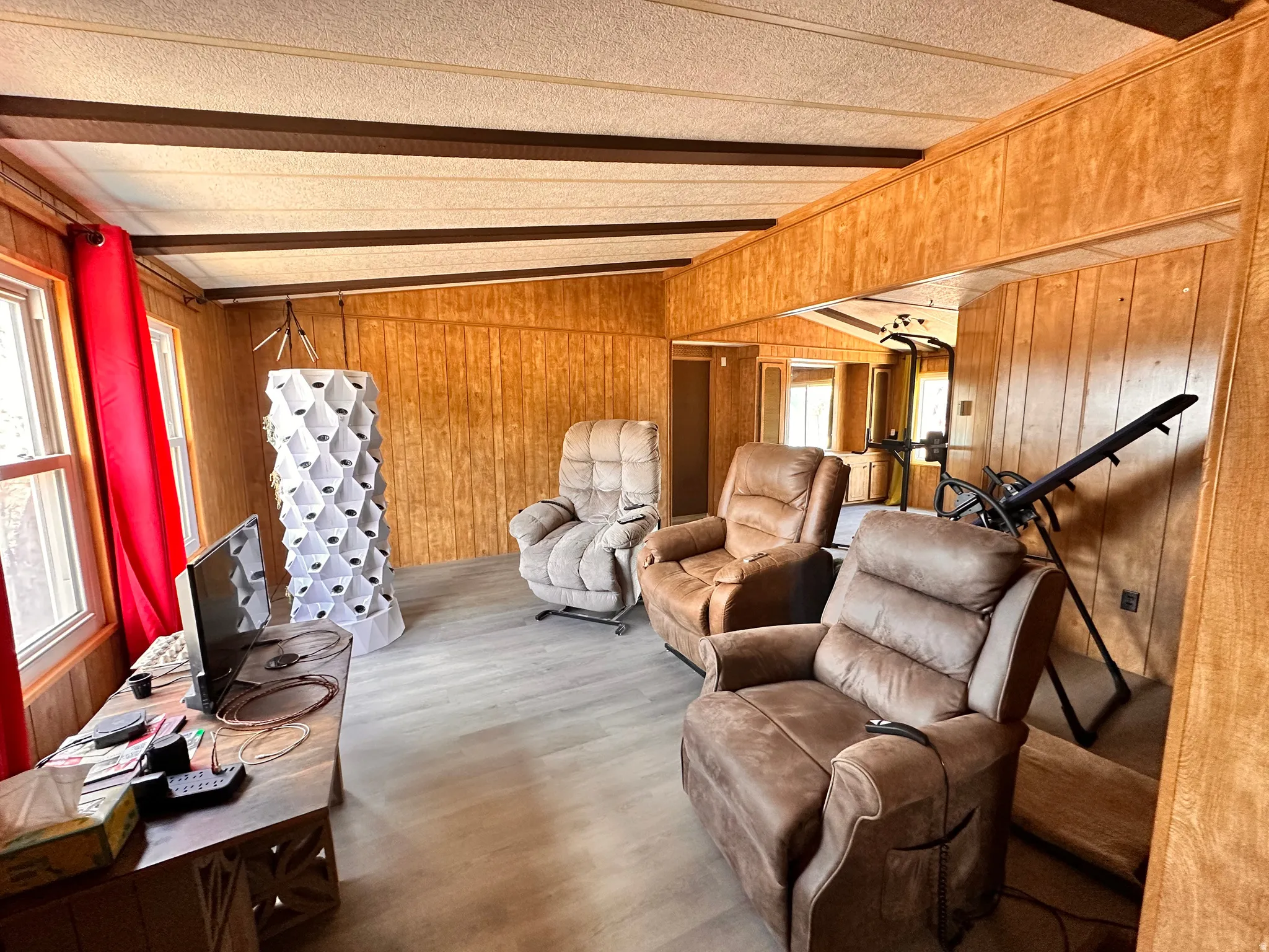 Room featuring light wood-finish flooring, wood paneling, multiple windows, and exposed ceiling beams