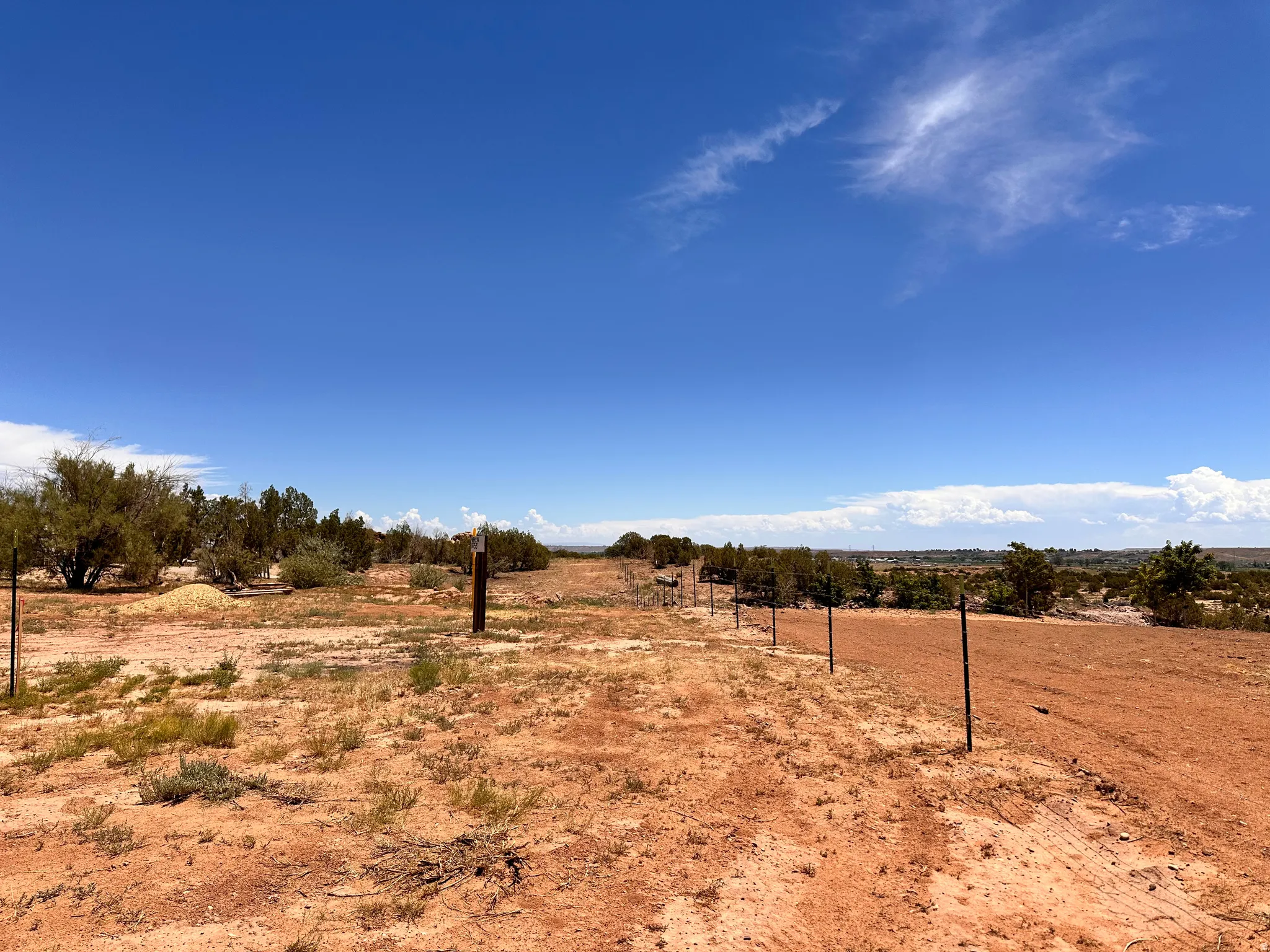Expansive undeveloped lot featuring red earth, scattered low-lying vegetation, and a clear blue sky
