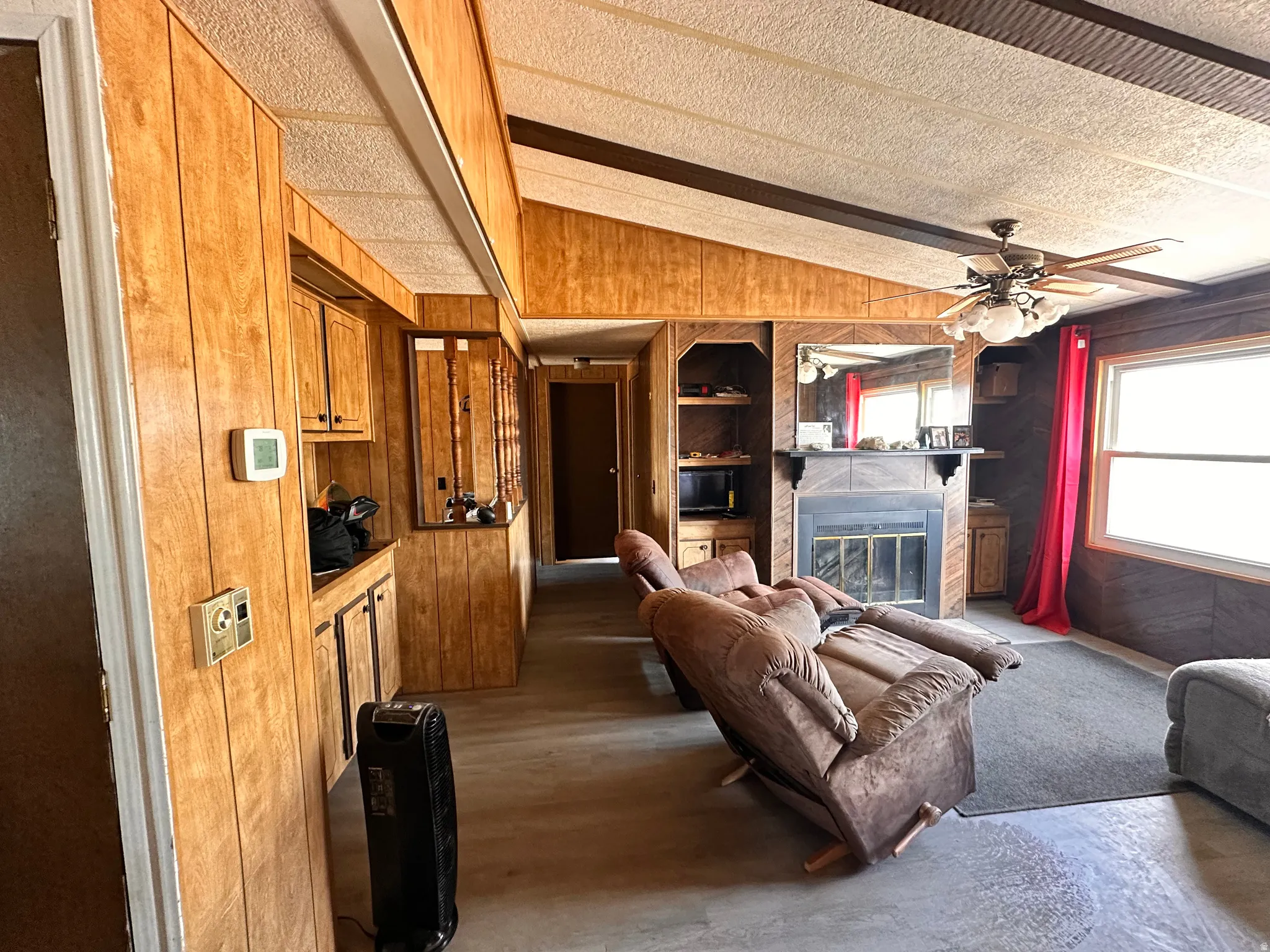 Living area featuring wood-finish paneling, a ceiling fan with integrated lighting, and a fireplace with a stone-look surround