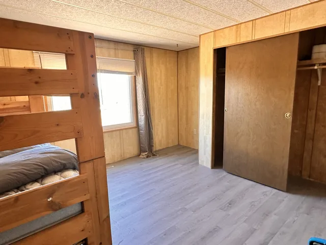 Room featuring wood-finish paneling, light wood-finish flooring, and a window with blinds