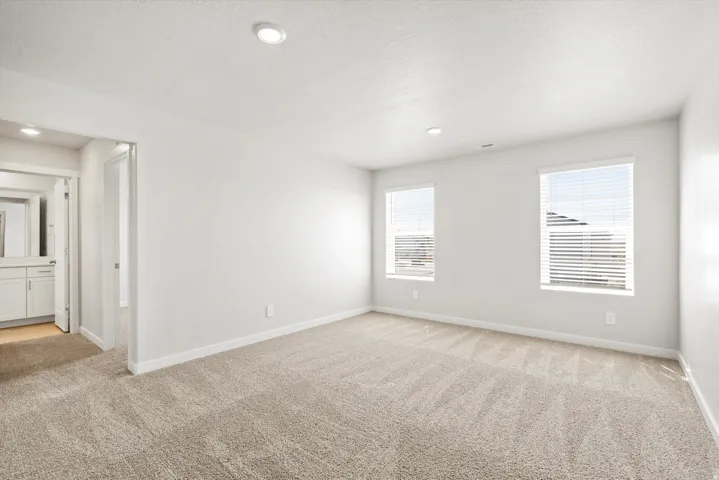 Spacious room featuring neutral carpeting, recessed lighting, and two windows with blinds