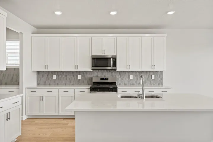 Modern kitchen featuring white cabinetry, a hexagonal tile backsplash, stainless steel appliances, and a central island with a double basin sink