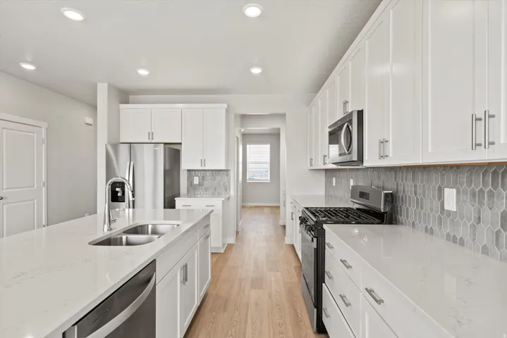 Modern kitchen featuring white shaker cabinetry, stainless steel appliances, and wood-finish flooring
