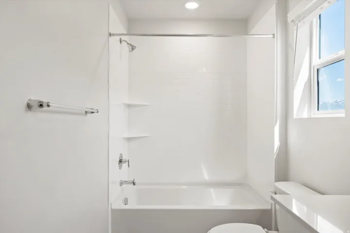 White tiled shower/tub combination with chrome fixtures, integrated shelving, and a bright window