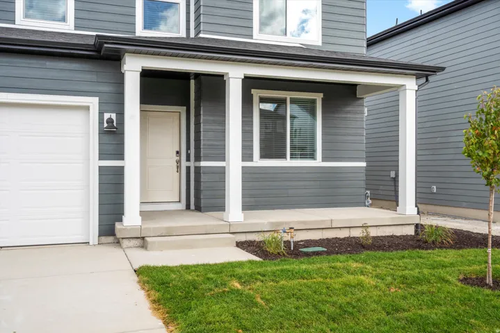 Front exterior featuring a covered porch with white columns, horizontal siding, a light-colored entry door, and an attached garage with a white door