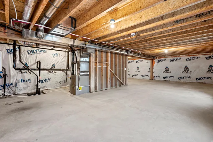 Unfinished basement featuring exposed wood joists, concrete flooring, and insulated walls