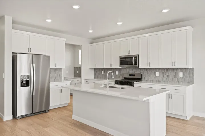 Kitchen featuring an expansive center island with an undermount sink, light-toned cabinetry, stainless steel appliances, a geometric tile backsplash, and wood-finish flooring