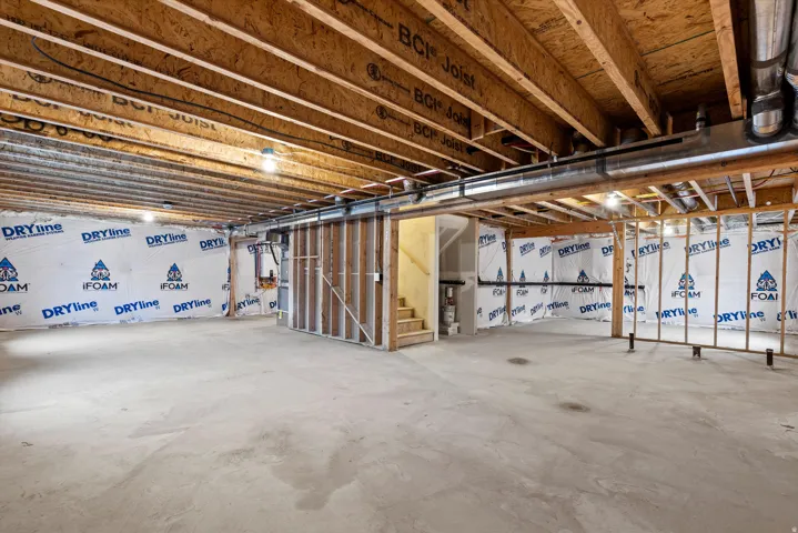 Unfinished basement featuring exposed wood joists and subflooring, concrete slab flooring, and framed interior walls with insulation backing