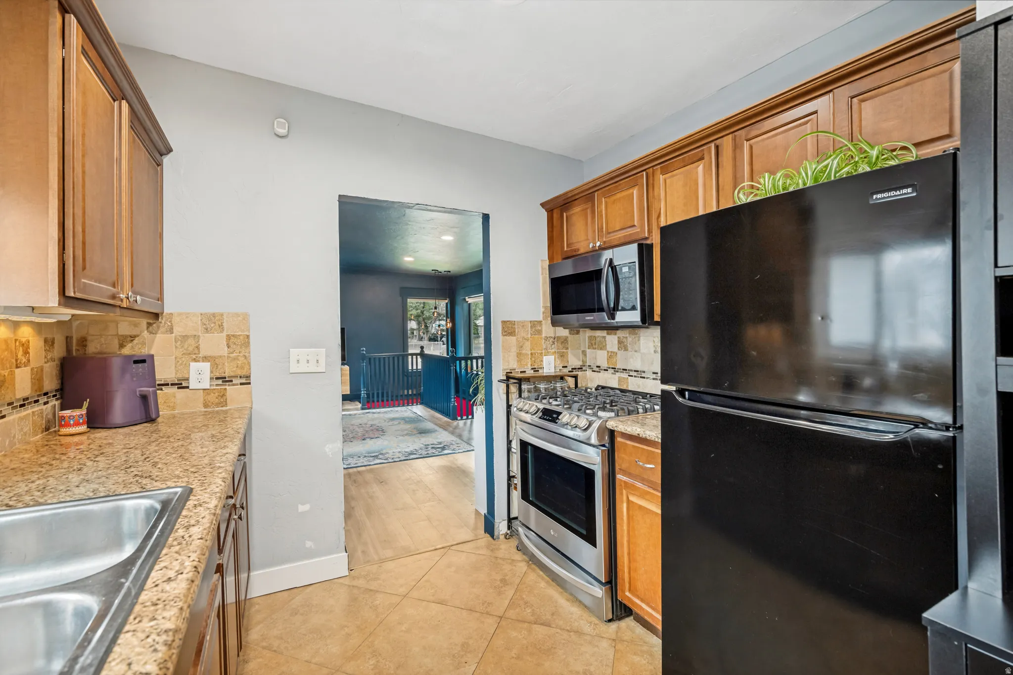 Kitchen featuring medium-tone wood cabinetry, granite countertops, a stainless steel gas range, and a black refrigerator