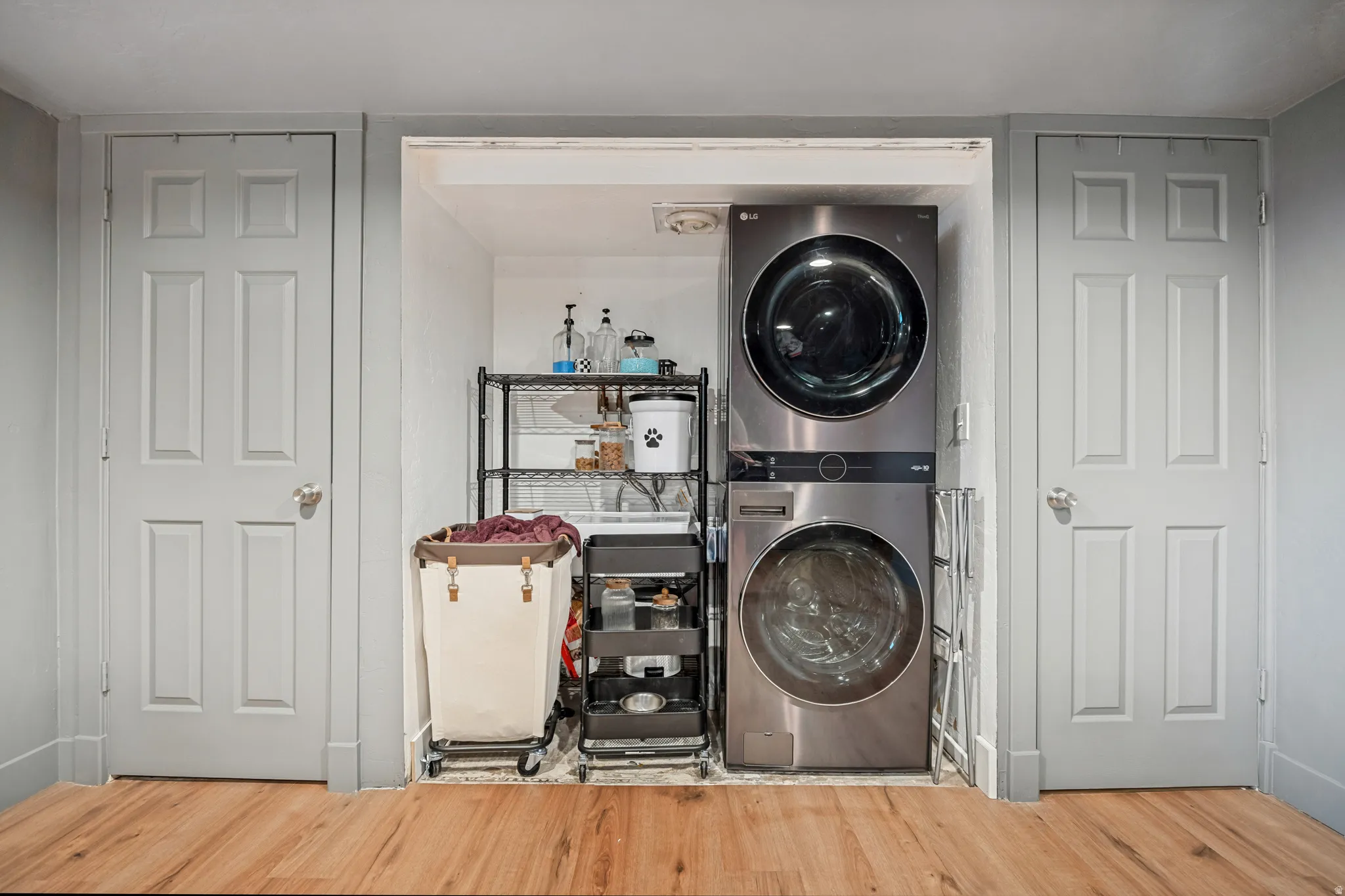 Dedicated laundry area featuring a stacked washer and dryer, wood-finish flooring, and light gray paneled doors