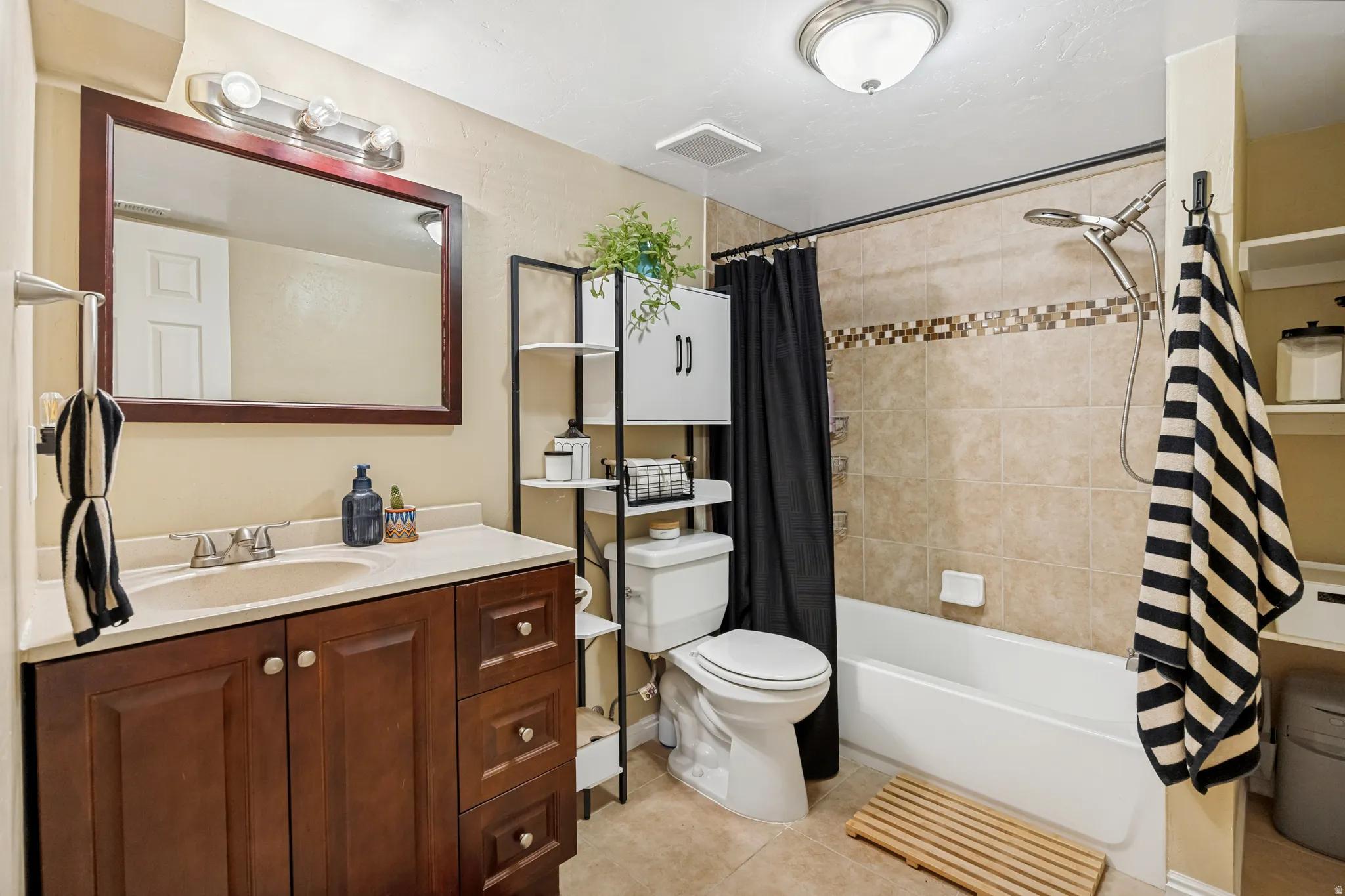 Bathroom featuring a dark wood-finish vanity with a light countertop, a framed mirror, a tub-shower combination with tiled surround, and recessed shelving